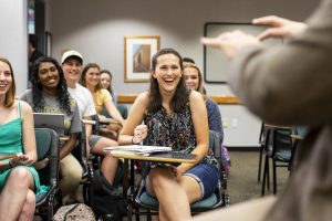 Classroom with students smiling and professor off to the side.