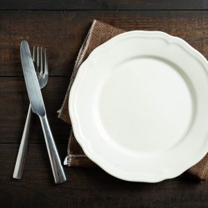 Empty white plate with utensils on wooden table.